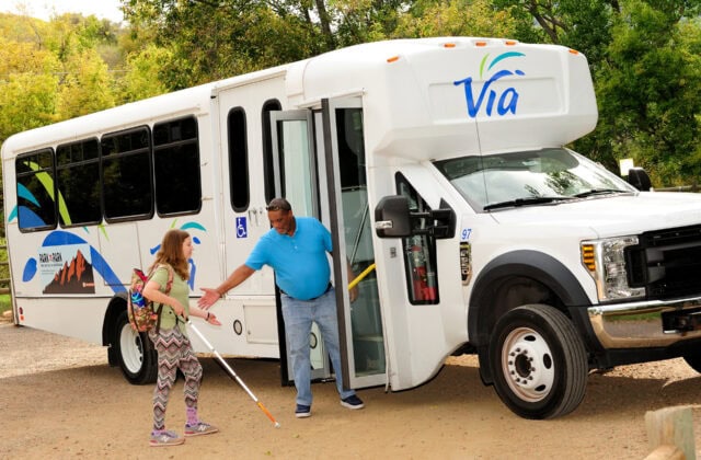 A driver helps a passenger into a Via Mobility Services shuttle.