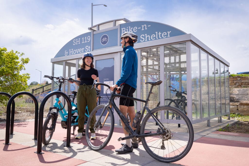 A woman and man standing next to their bikes in front of a Bike-n-Ride shelter