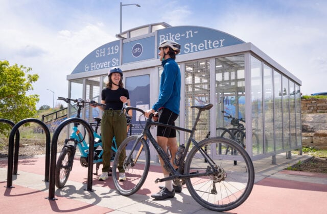 A woman and man standing next to their bikes in front of a Bike-n-Ride shelter