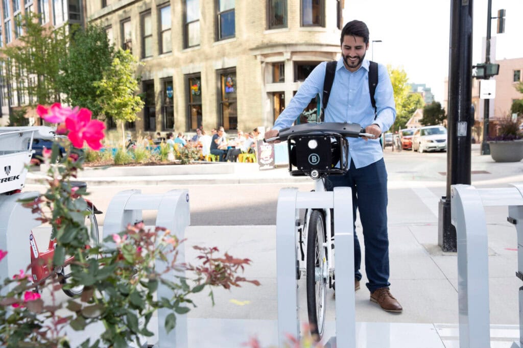Man wearing button down shirt and backpack returning bike to a bike share kiosk